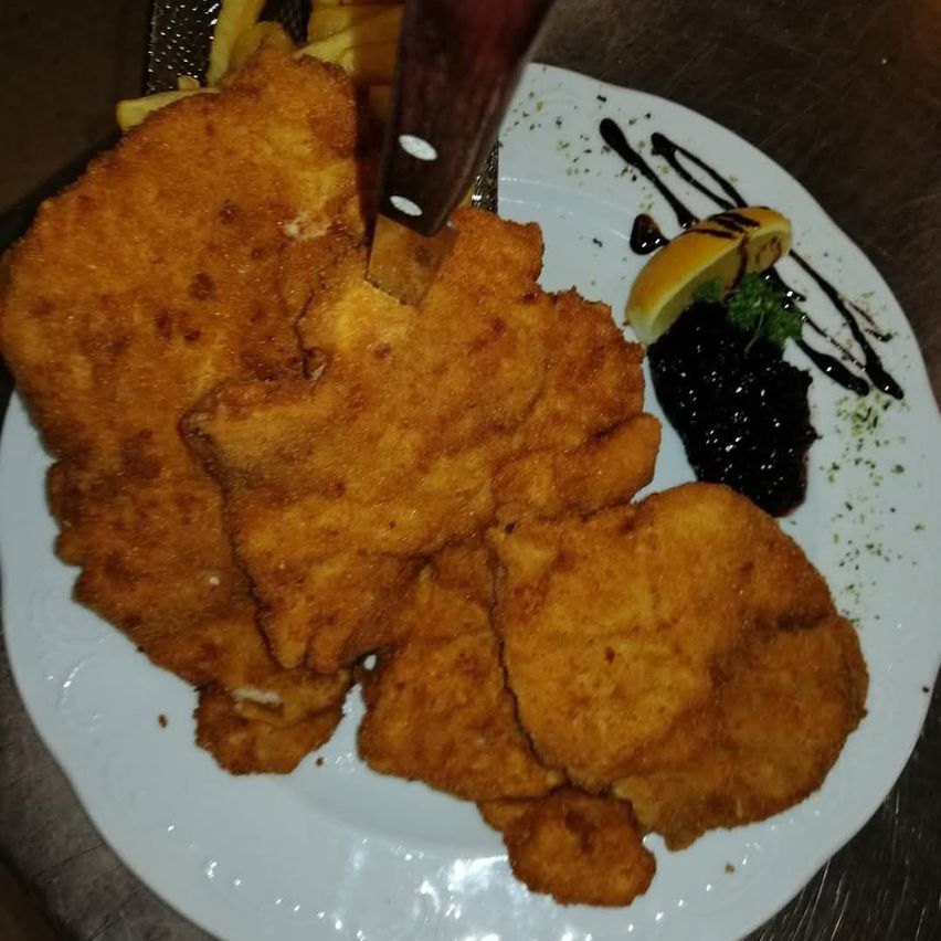 Ein Teller mit gebratenem paniertem Fleisch mit einem Messer, serviert mit einer Beilage aus Pommes Frites, schwarzem Kaviar und einer Zitronenscheibe.