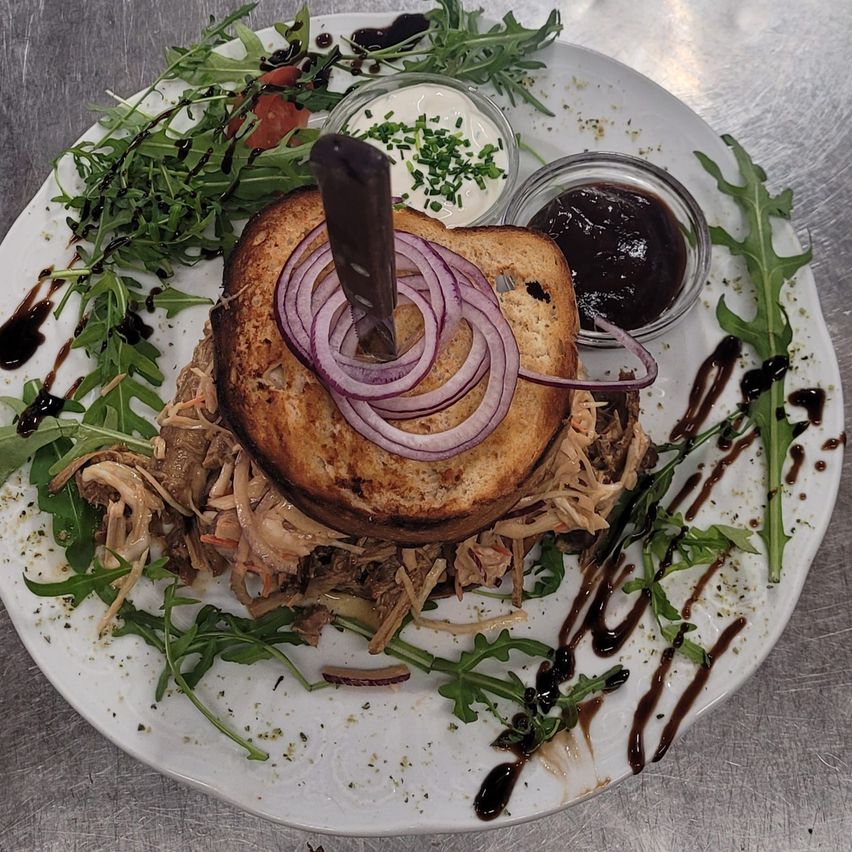 A sandwich with a slice of meat and onion on a white plate with a sauce and garnishes.