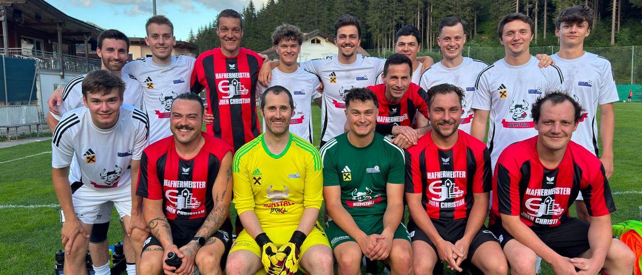 Eine Gruppe von Fußballspielern in verschiedenen Teamtrikots posiert für ein Foto auf einem Rasenfeld mit Bergen im Hintergrund.