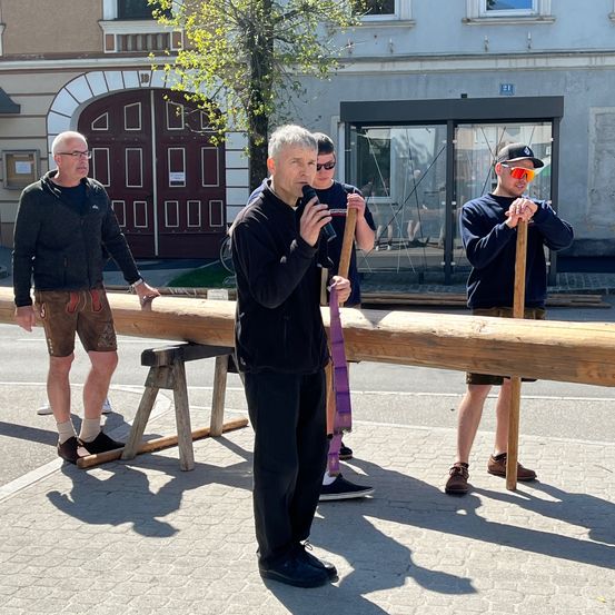Eine Gruppe von Männern auf der Straße, einer spricht in ein Mikrofon, während andere Holzstangen halten.
