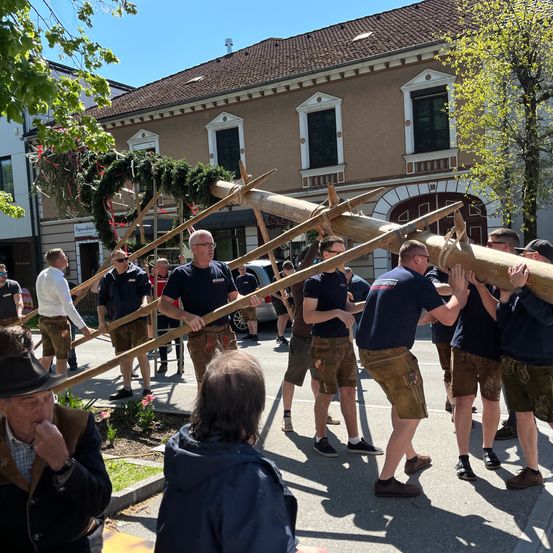 Eine Gruppe von Männern hebt gemeinsam einen langen Gegenstand in der Straße an. Sie tragen traditionelle Kleidung.