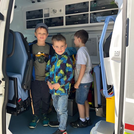 Drei Jungen stehen in einem Krankenwagen. Zwei von ihnen lächeln, und einer hält einen Rucksack.