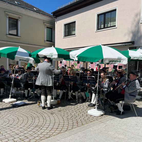 Ein Blasorchester spielt auf der Straße mit grünen und weißen Schirmen vor ihnen.