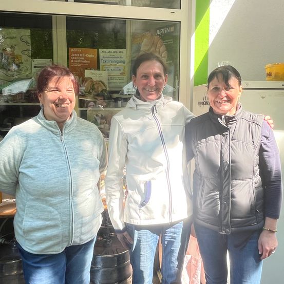 Drei Frauen stehen nebeneinander vor einer Bäckerei. Die Frau auf der linken Seite lächelt.