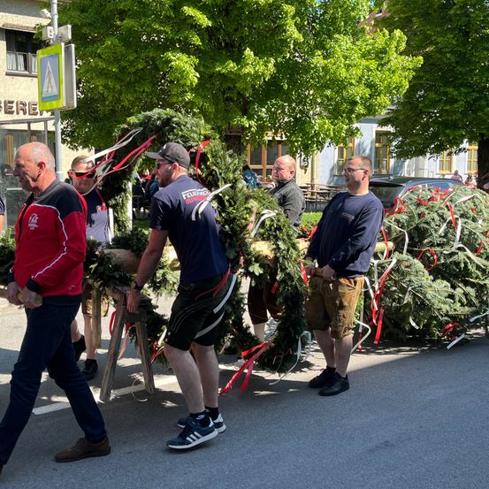 Eine Gruppe von Männern steht neben einem Weihnachtsbaum und trägt Kränze und Bänder.