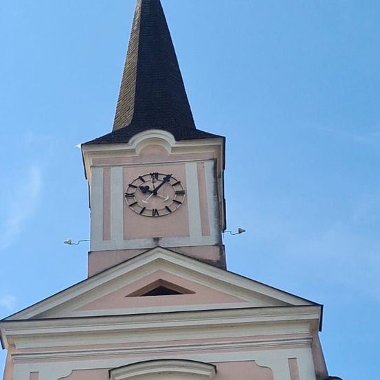 Ein rosafarbener Kirchturm mit einer Uhr, die 10:45 Uhr anzeigt, unter einem klaren blauen Himmel.