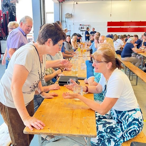Eine Gruppe von Menschen sitzt in einer Cafeteria an Tischen, einige lächeln und unterhalten sich, mit Gläsern und Tellern auf den Tischen.