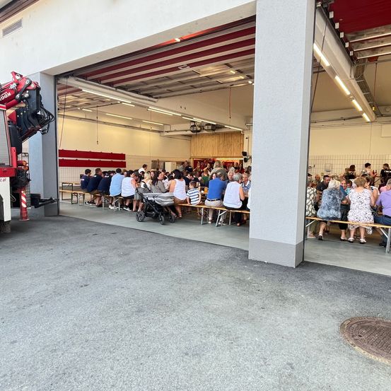 Eine Gruppe von Menschen sitzt auf Bänken in einer Feuerwache, einige tragen Hüte und Schuhe.