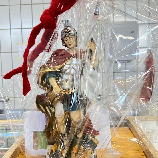 Eine Statue eines römischen Soldaten in Rüstung, mit Helm und Speer in der Hand, ist in Plastik verpackt. Der Soldat steht auf einem Holztisch.