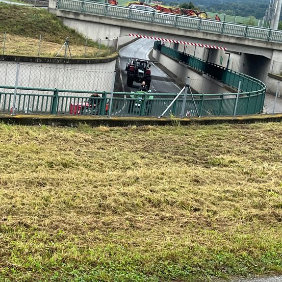 Eine Straße mit geparkten Maschinenfahrzeugen in der Nähe einer Brücke mit Zaun und Barriere.