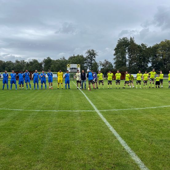 Eine Fußballmannschaft steht auf einem Feld, das von einem bewölkten Himmel und Bäumen im Hintergrund umgeben ist.