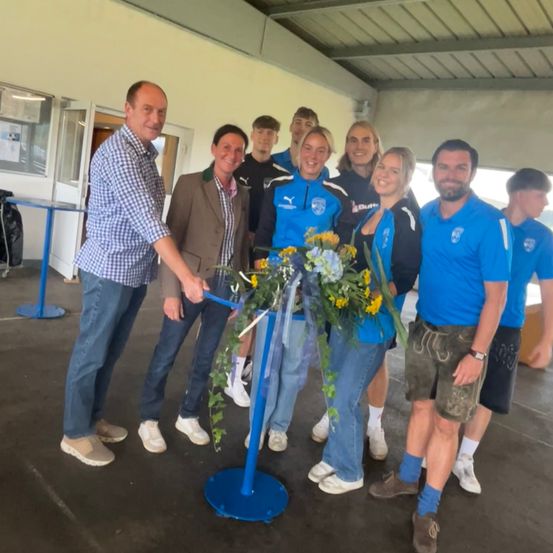 Eine Gruppe von Menschen in gleichen Uniformen steht bei einer Schleifchen-Schneidzeremonie, lächelt und posiert für ein Foto.