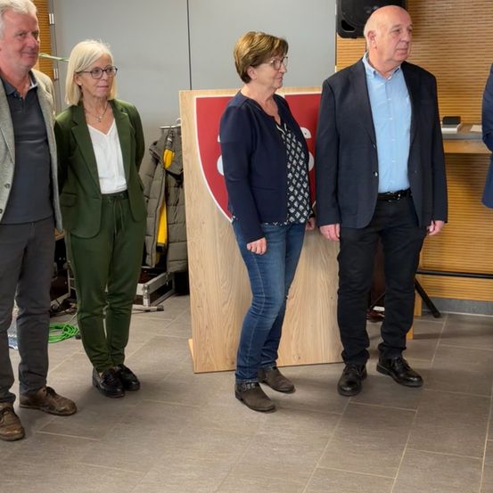 Vier Personen stehen neben einem hölzernen Podium mit einem roten und weißen Schild darauf. Sie sind geschäftlich gekleidet.