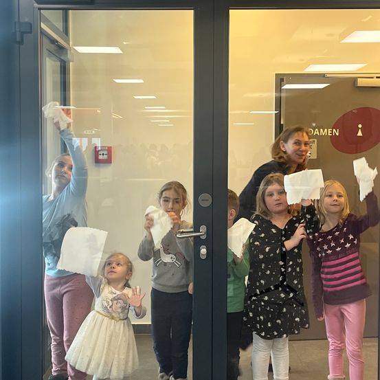 Eine Gruppe junger Mädchen hält Papierhandtücher in der Hand und lächelt, während sie vor einer Glastür stehen, an der eine Tafel mit Damen steht.