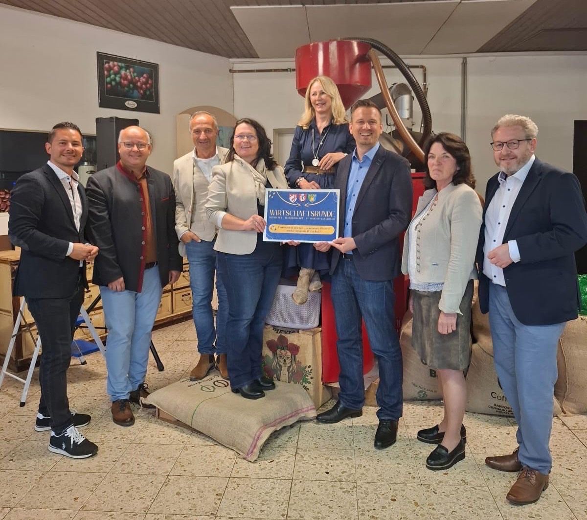 Eine Gruppe von Menschen, darunter Männer und Frauen, steht in einem Fabrikraum. Sie lächeln und scheinen für ein Foto zu posieren. Eine Frau hält ein Zertifikat in der Mitte.