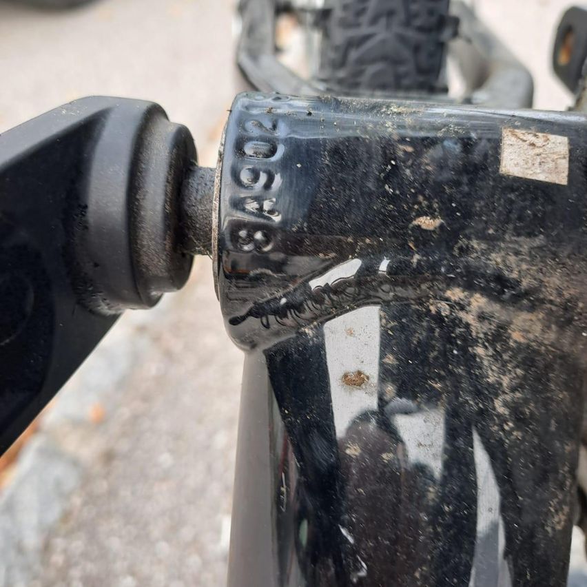 Nahaufnahme der hinteren Fahrradfederung mit sichtbarem Schmutz und Kratzern, einschließlich der Nummer 834930 auf dem Metall.