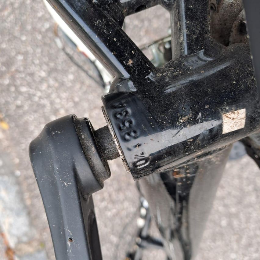 Eine Nahaufnahme des Hinterrads eines Fahrrads zeigt eine schwarze, rostige Metallstruktur mit einer gravierten Seriennummer 23564 und einem Identifikationsaufkleber.