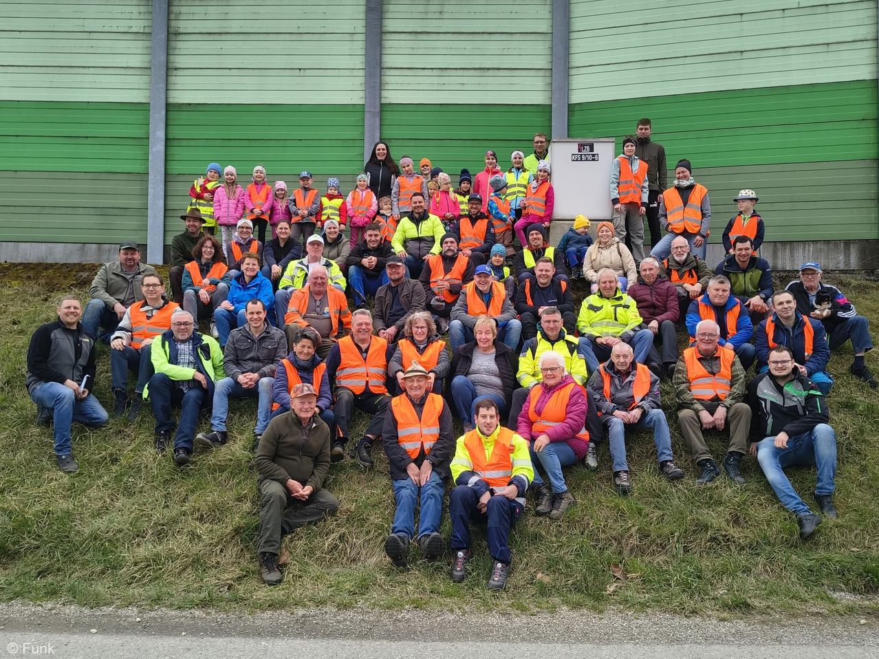 Eine Gruppe von Menschen in Warnwesten posiert für ein Foto vor einer grünen Wand.