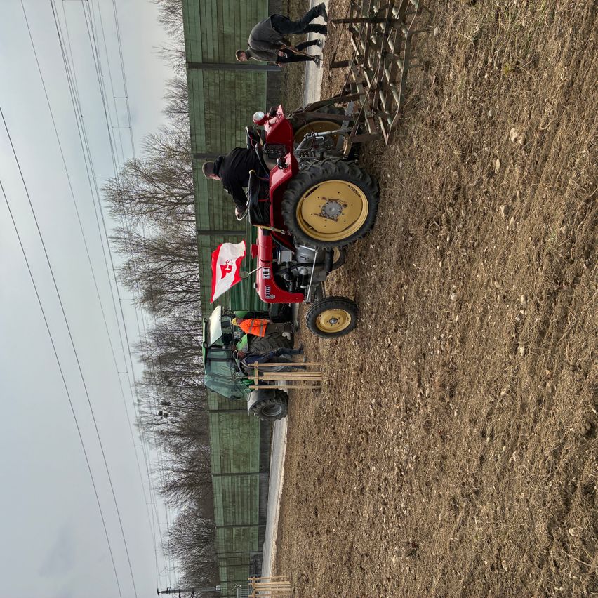 Ein Luftbild von zwei Traktoren, die in einem Feld geparkt sind, mit Arbeitern in der Nähe, einer mit einer Flagge.