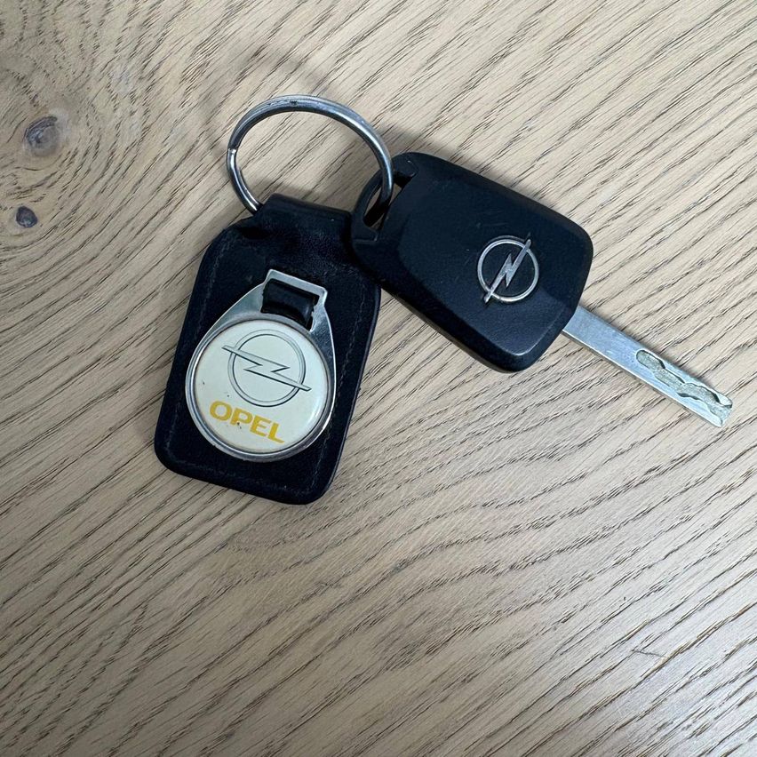 Zwei Opel-Autoschlüssel auf einem Holztisch. Der Schlüssel zeigt das Opel-Logo auf dem Schlüsselanhänger.
