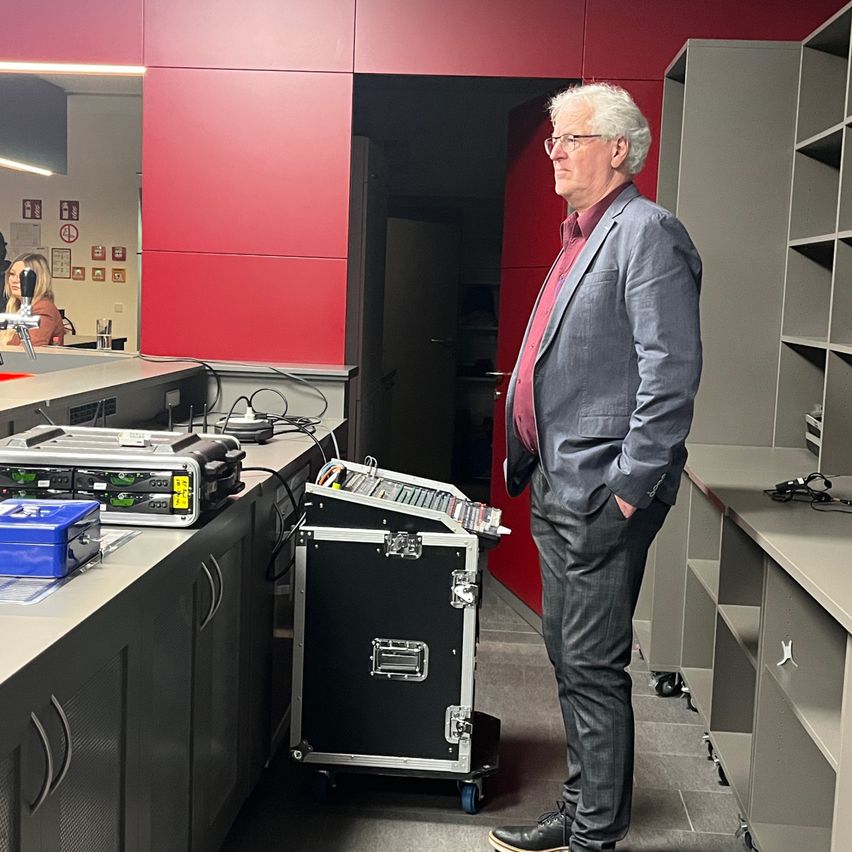 An older man in a suit is standing in a room, looking at equipment on the table.