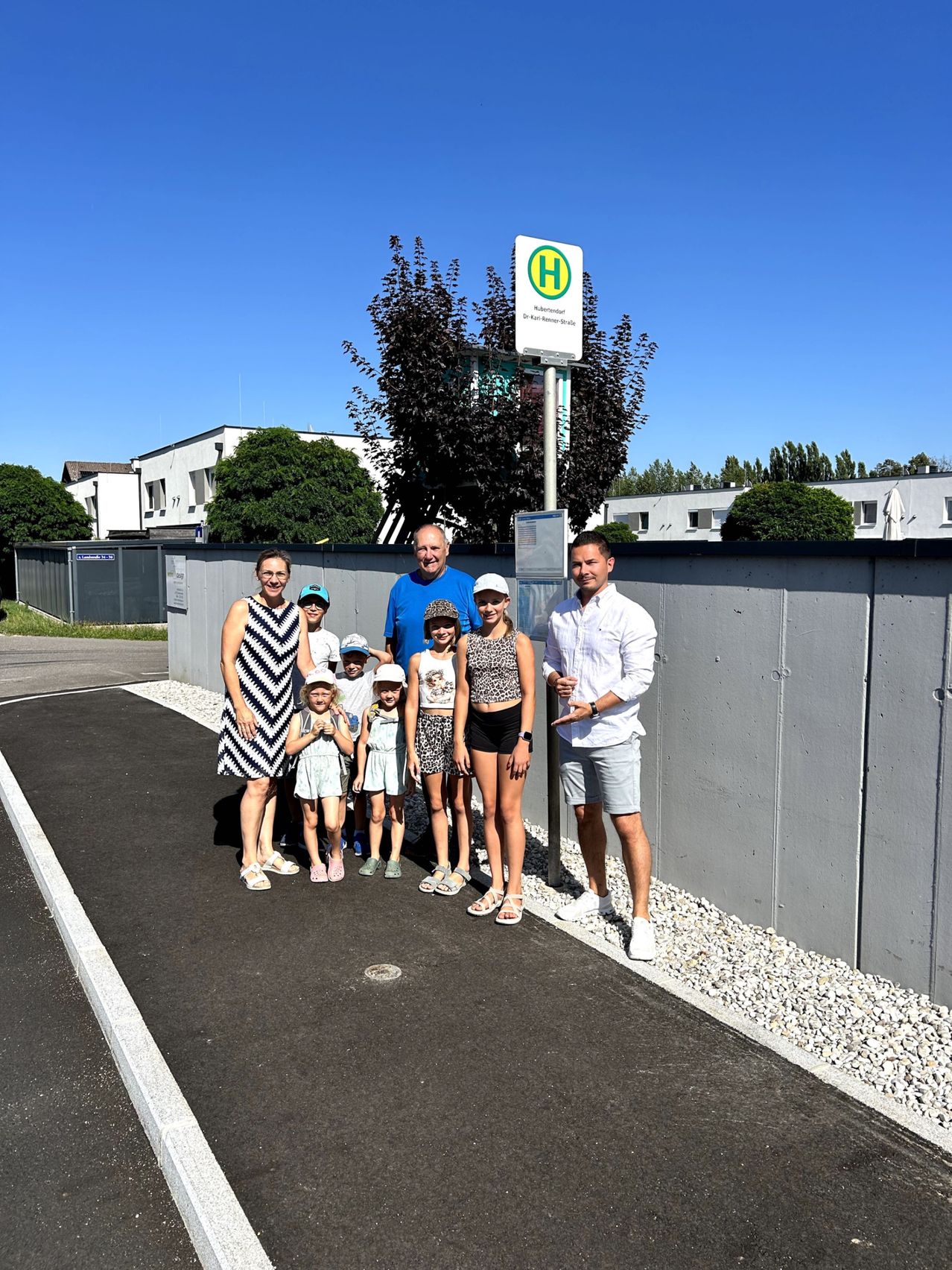 Eine Familie von acht Personen, einschließlich Erwachsener und Kinder, steht vor einer Betonmauer mit einem Schild. Die Kinder tragen Hüte und Turnschuhe.