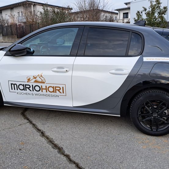 Die Seite eines schwarzen und weißen Autos mit dem Text Mario Hari Küchen und Wohndesign.