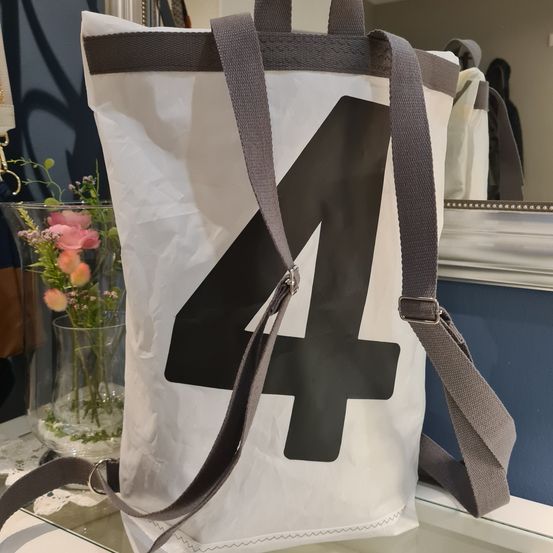 Ein weißer Beutel mit schwarzer Nummer 4, auf einem Tisch ausgestellt, mit einem Glasvase mit rosa Blumen dahinter.