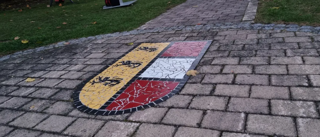 Ein zerbrochenes schildförmiges Mosaik auf einem Ziegelweg im Park.