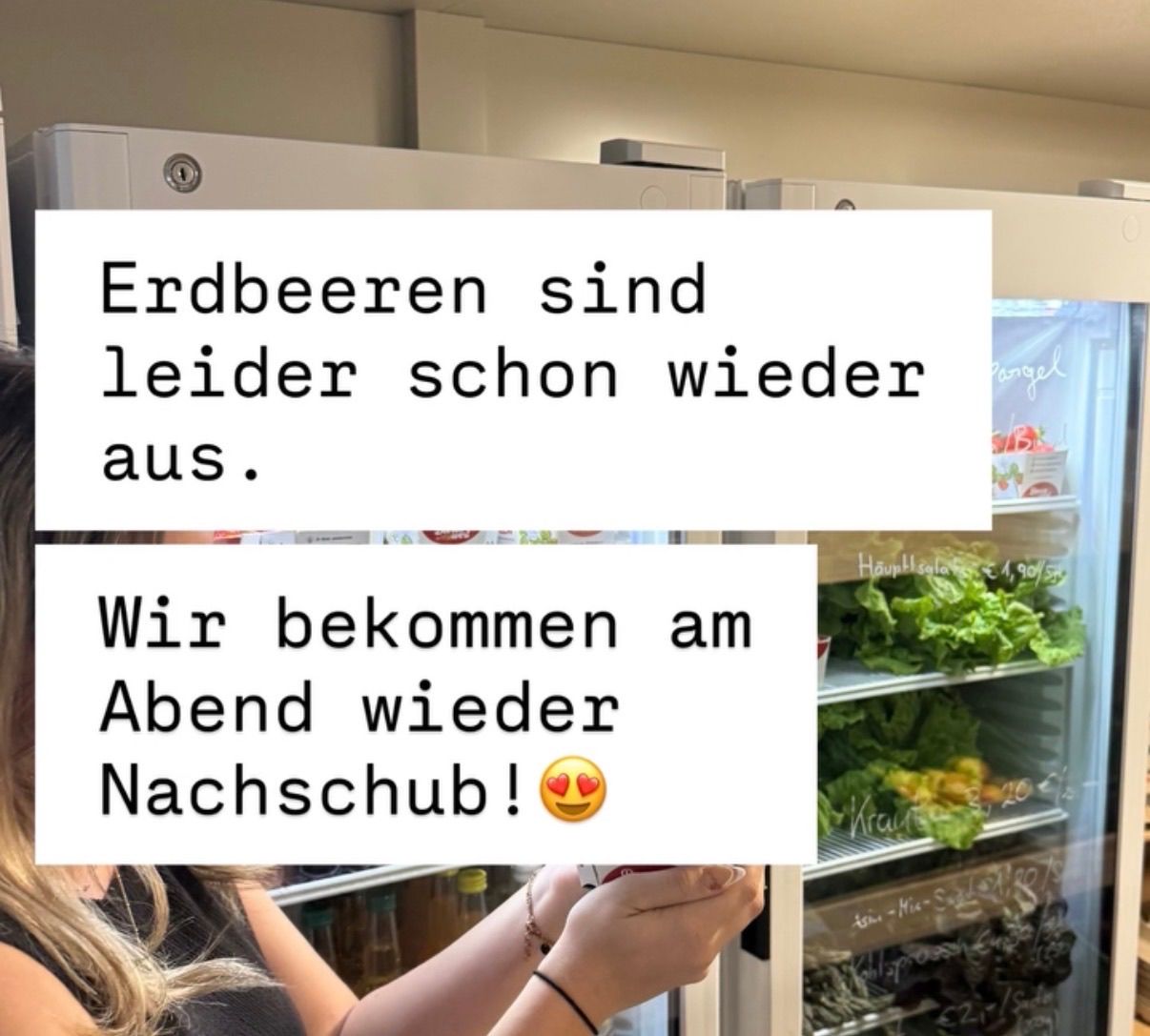 Eine Person steht vor einem Kühlschrank mit dem Text: 'Erdbeeren sind leider schon wieder aus. Wir bekommen am Abend wieder Nachschub!' Im Inneren befinden sich Gemüse.