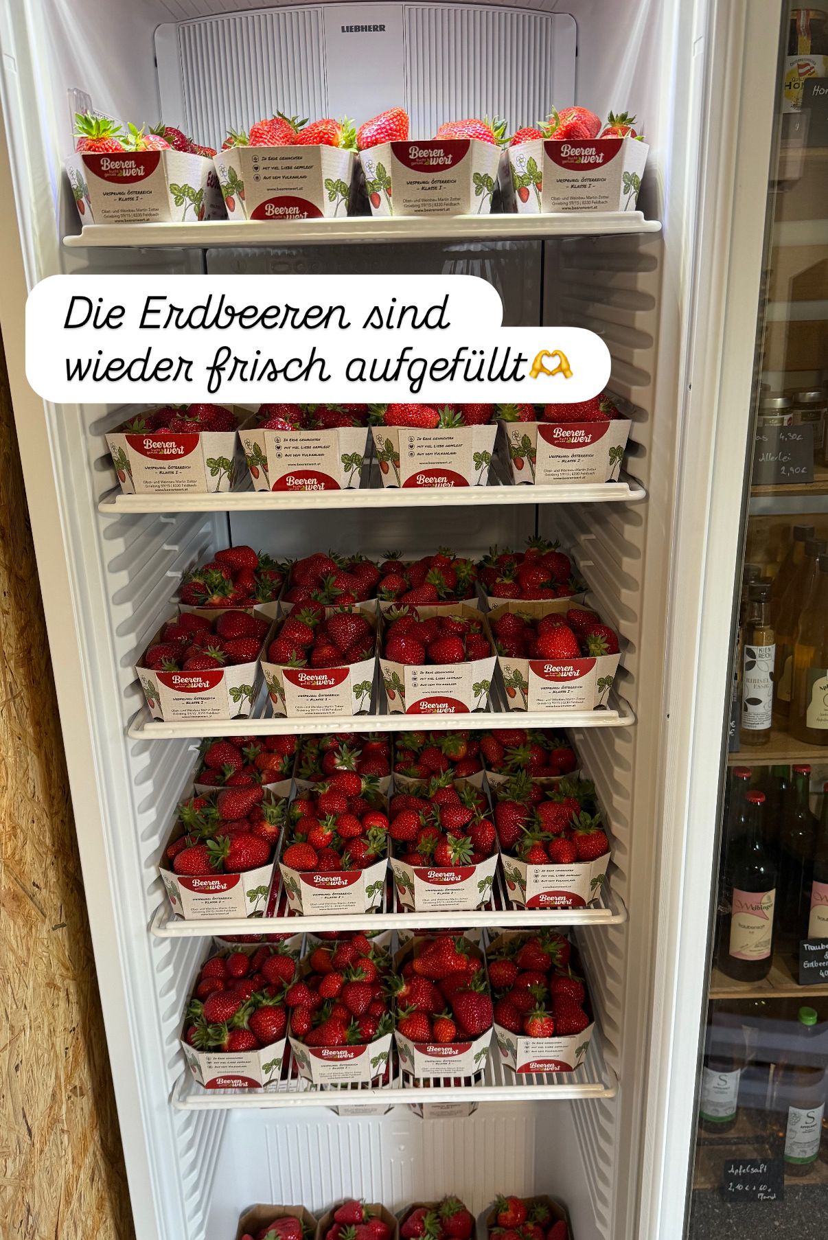 A refrigerator full of strawberries, neatly arranged in boxes labeled 'Beeren'. A note reads 'Die Erdbeeren sind wieder frisch aufgefüllt', meaning 'The strawberries are freshly refilled'.