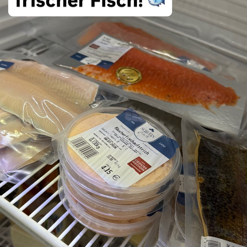 Ein Nahaufnahme eines Kühlschrankregals mit verschiedenen verpackten Fischprodukten, darunter ein Stapel Lachsfilets und ein Behälter mit geräuchertem Fisch.