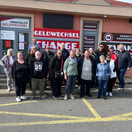 Eine Gruppe von Menschen steht vor einem Gebäude mit den Worten 'CHANGE' und 'GELDWECHSEL' darauf. Sie tragen Winterkleidung und scheinen für ein Foto zu posieren.