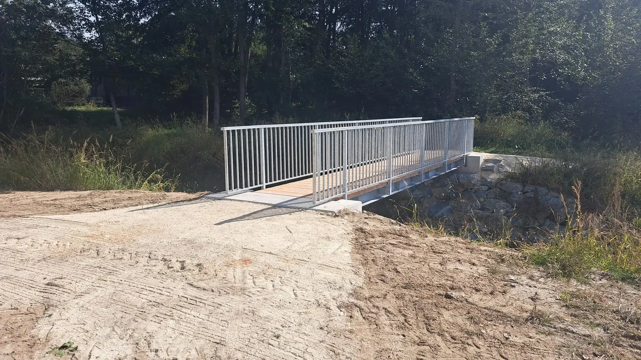 Eine Fußgängerbrücke aus Metall wird über einem Erdweg errichtet.