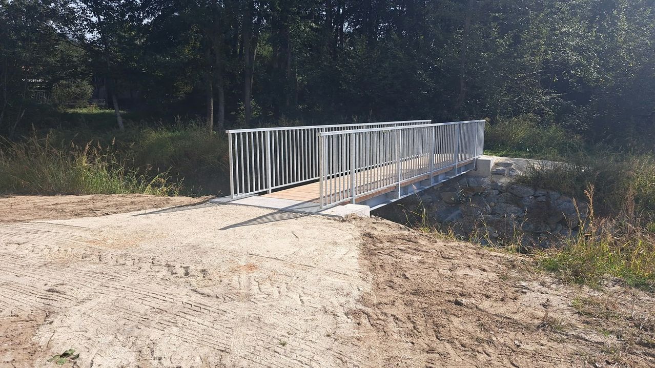 Eine Fußgängerbrücke aus Metall wird über einem Erdweg errichtet.