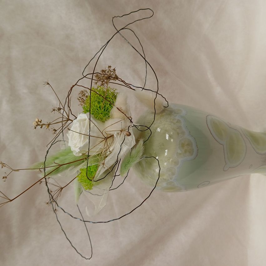 Eine klare Glasvase mit weißen und grünen Blumenarrangements steht auf einem weißen Hintergrund. Die Vase hat ein abstraktes Design mit grünen Wirbeln.