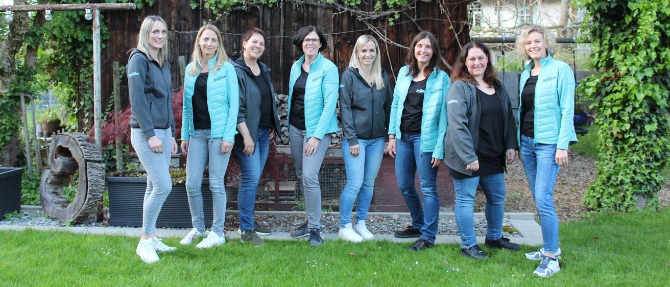Eine Gruppe von Frauen in blauen Jacken und Jeans posiert für ein Foto vor einem Holzhaus.