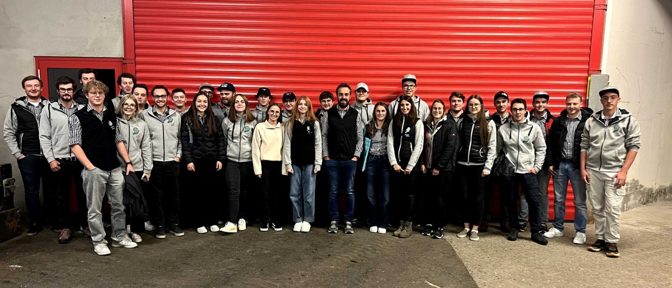 Eine Gruppe von Menschen in passenden Jacken steht vor einer roten Garagentür.