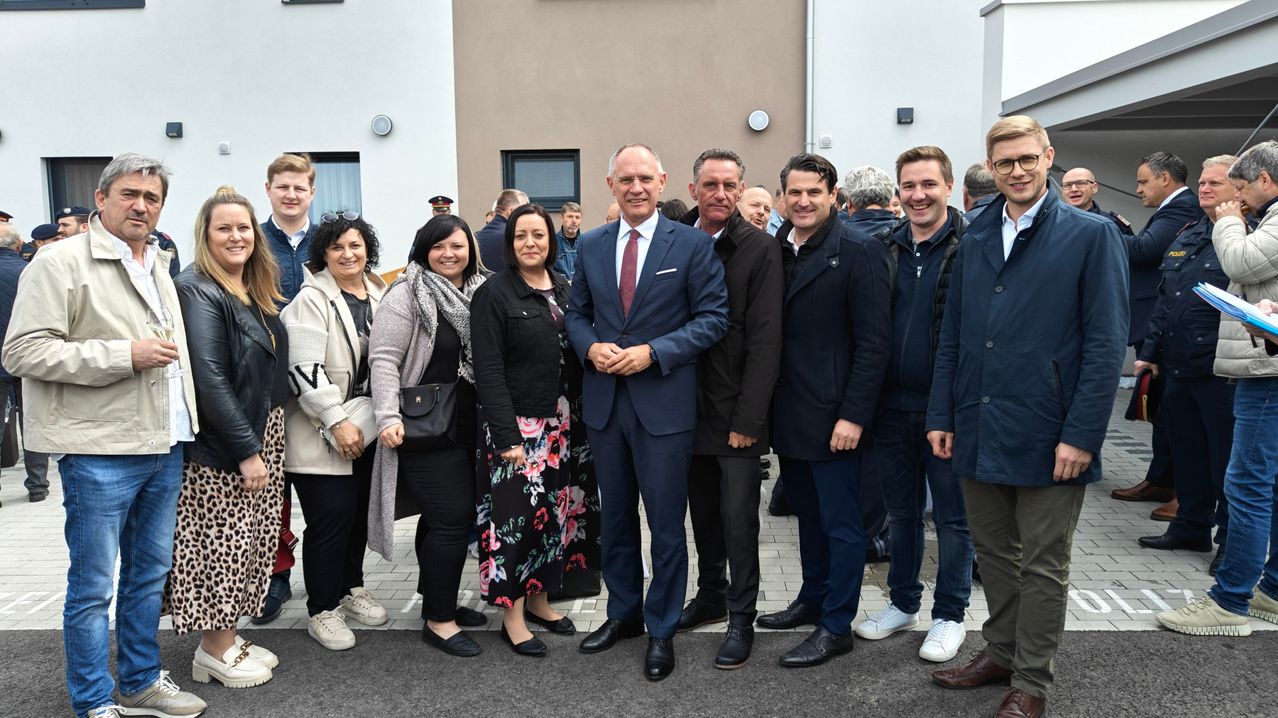 Eine Gruppe von Menschen, darunter ein Mann im Anzug, steht lächelnd vor einem Gebäude.