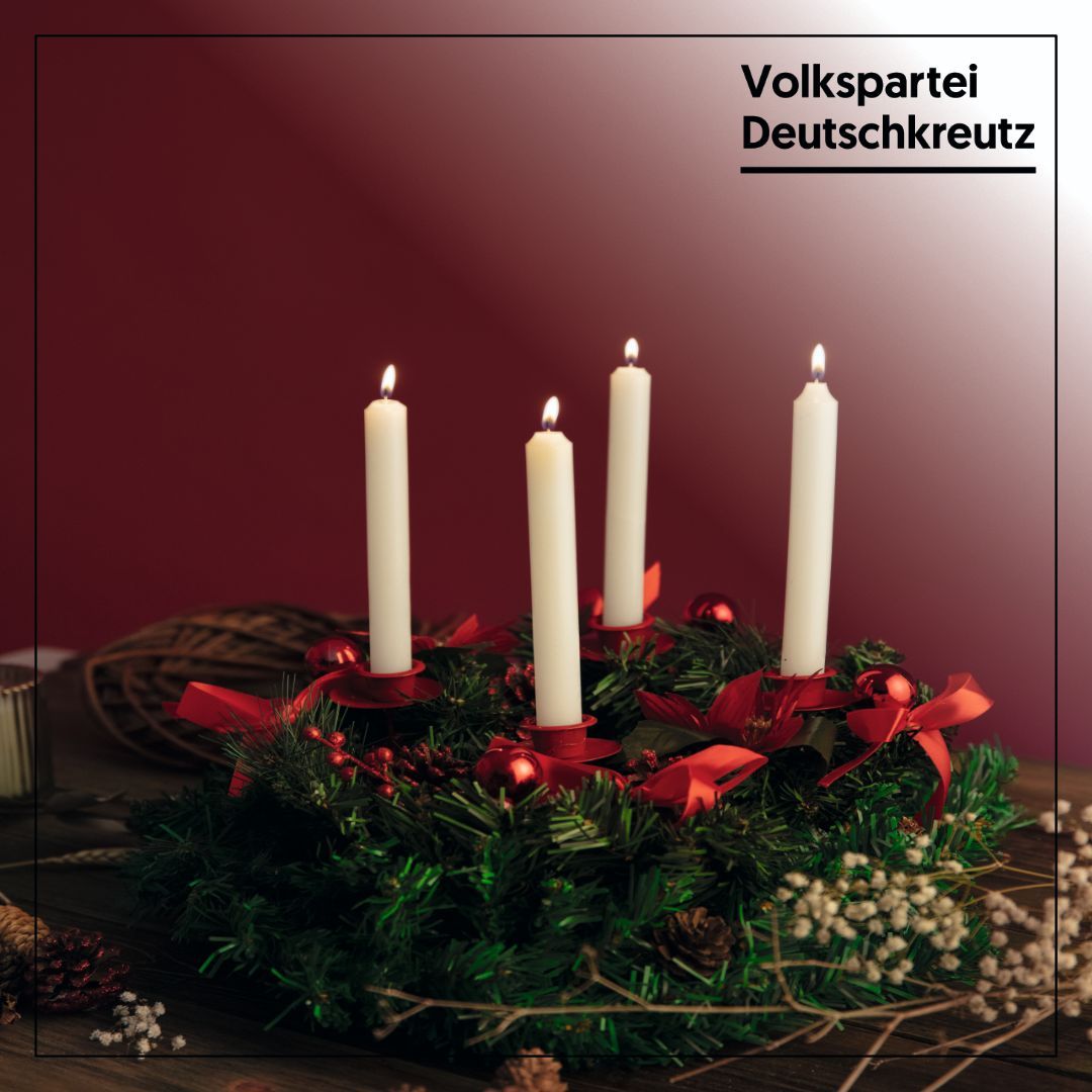 Ein Kranz mit vier weißen Kerzen, dekoriert mit roten Bändern und Weihnachtsdekorationen, vor einem dunkelroten Hintergrund.