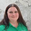 A woman with long brown hair wearing a green polo shirt with a white logo on the left chest area.