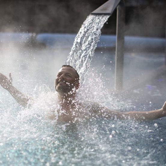 Ein Mann genießt einen Moment in einem Whirlpool, um den ihn Wasser spritzt. Das Wasser ist klar und blau.