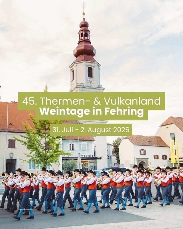 Eine Blaskapelle in roten und weißen Uniformen spielt Instrumente vor einem Kirchturm. Das Ereignis ist der 45. Thermen- & Vulkanland Weintage in Fehring, geplant für den 31. Juli bis 2. August 2026.