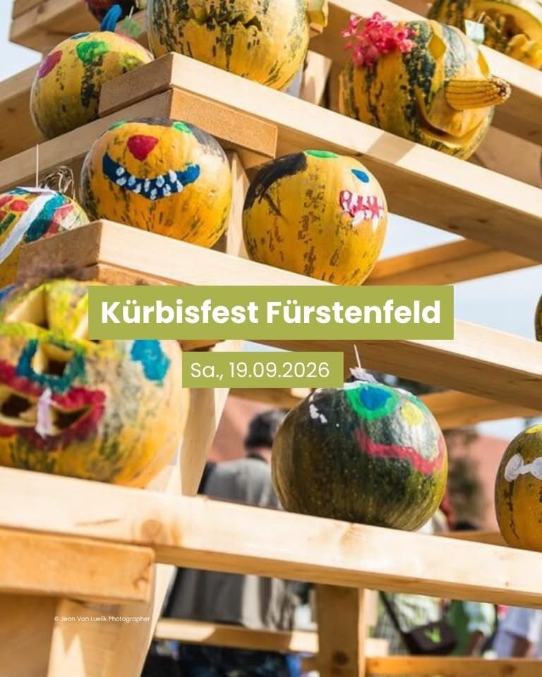 Ein Holzregal zeigt bunt bemalte Kürbisse mit Gesichtern, vor dem Hintergrund eines Kürbisfestes in Furstenfeld am 19. September 2026.