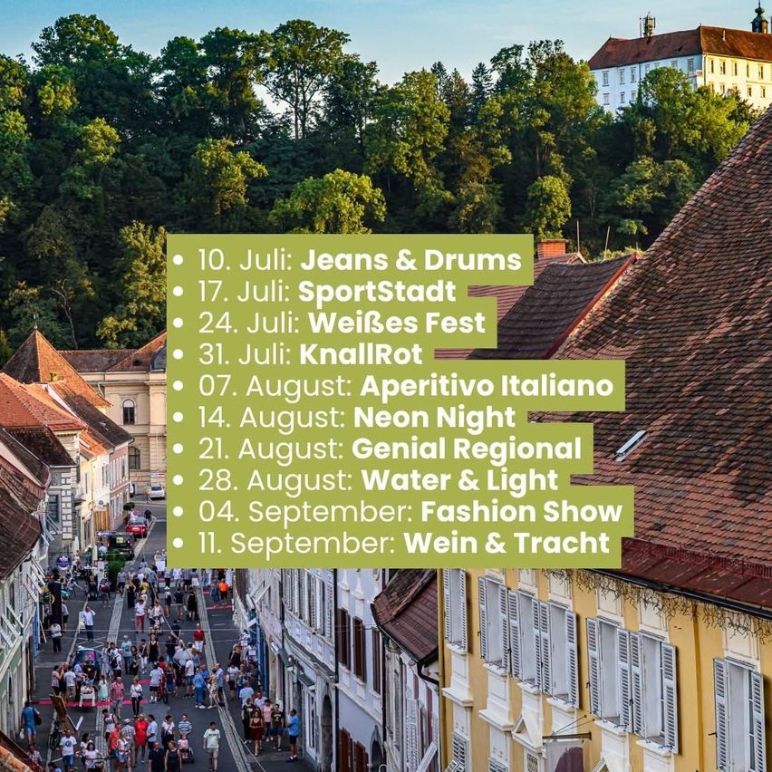 Ein Straßenfest mit Gebäuden und einer Menschenmenge. Ein grünes Banner listet mehrere Veranstaltungen auf, darunter Jeans & Drums und SportStadt.
