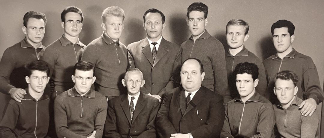 Ein Schwarz-Weiß-Foto einer Gruppe von Männern, einige in Anzügen und andere in Sportkleidung, posieren für ein Foto in einer formellen Umgebung.