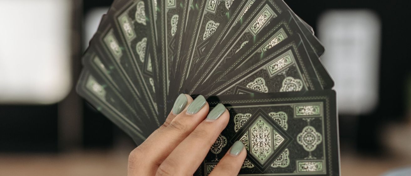 Eine Person mit grün lackierten Nägeln hält einen Stapel grün gestalteter Spielkarten in der Hand, möglicherweise für ein Spiel oder zur Wahrsagerei.