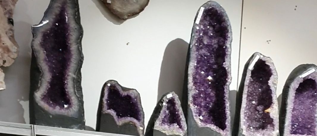 Eine Sammlung von Amethyst-Geoden ist auf Regalen ausgestellt. Eine Buddha-Statue befindet sich in der Mitte. Jeder Geode hat eine einzigartige Form und Farbe.