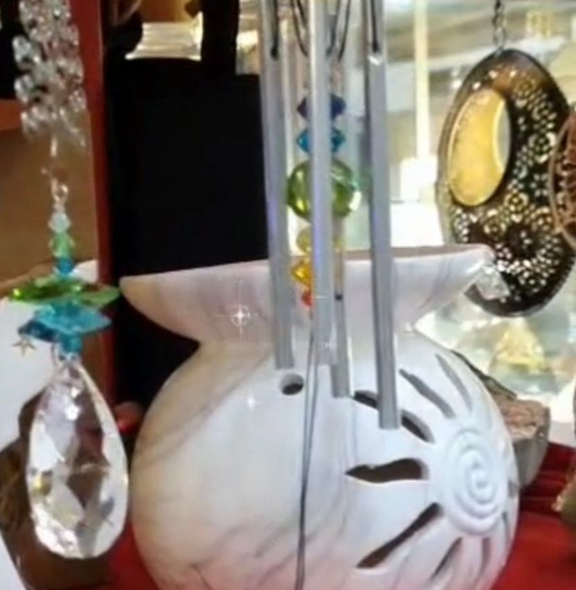 Eine weiße Keramikwindglocke hängt mit bunten Glasperlen, einem Spiraldesign auf dem Körper und einem Kristallanhänger in einem Geschäft.