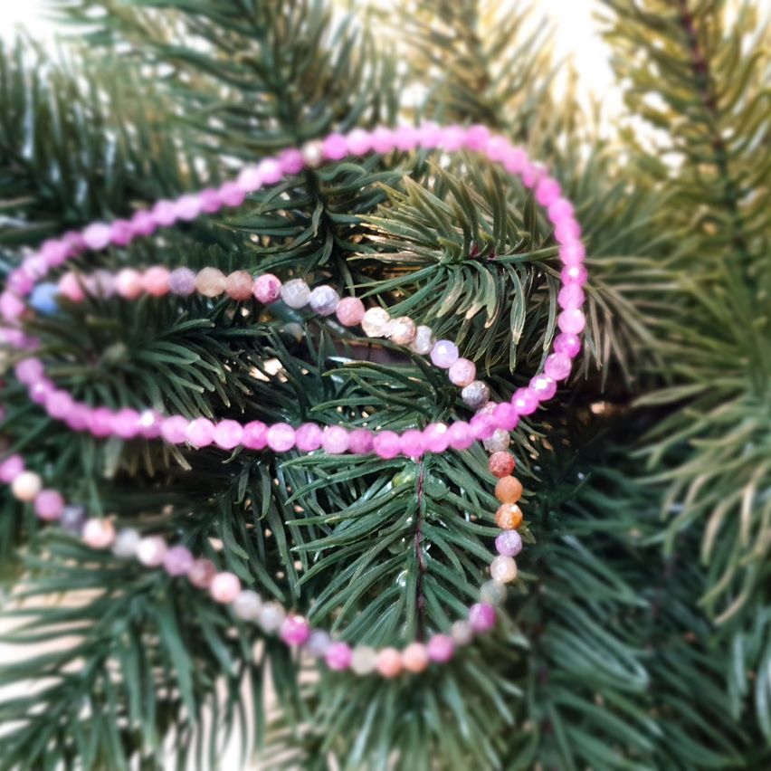 Zwei rosafarbene Perlenarmbänder liegen auf einem Weihnachtsbaum mit grünen Nadeln. Die Perlen variieren in Farbe, einschließlich rosa, weiß und orange. Der Baum ist leicht verschwommen.
